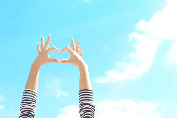 Las manos de la mujer joven haciendo marco en forma de corazón sobre fondo de cielo azul —  Fotos de Stock