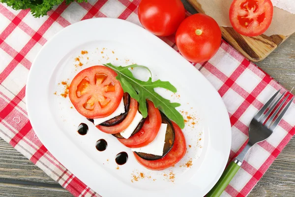 Eggplant salad with tomatoes and feta cheese on plate, on napkin,  on wooden background — Stock Photo, Image