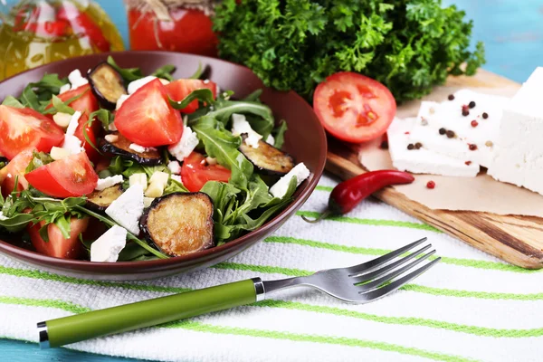 Eggplant salad with tomatoes, arugula and feta cheese, on napkin, on color wooden background — Stock Photo, Image