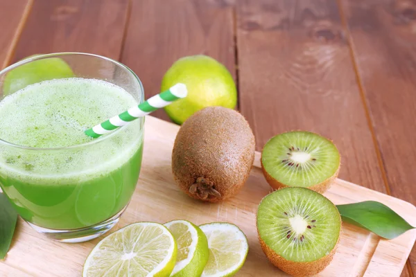 Glass of fresh lime juice with pieces of lime and kiwi on cut board and wooden table background