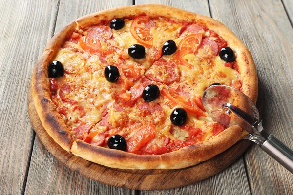 Ízletes pizza fekete olajbogyó és a kerek kést, és fából készült asztal háttere — Stock Fotó