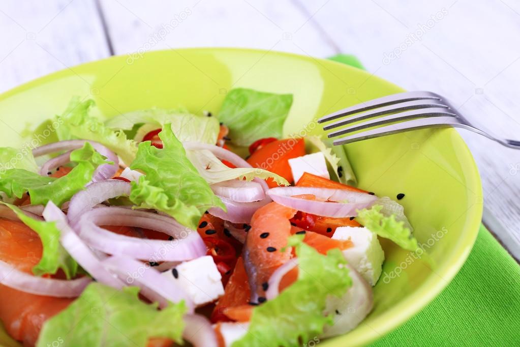 Fresh fish salad with vegetables on plate on wooden table close-up