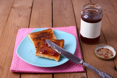 Plaka ve peçete reçel kavanoz ahşap masa arka plan üzerinde yakınındaki bıçakla yayılmış tost ekmeği