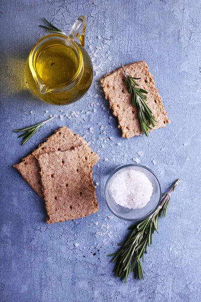 Knäckebröd med salt, kannan olja och kvistar rosmarin på färg träbord bakgrund — Stockfoto