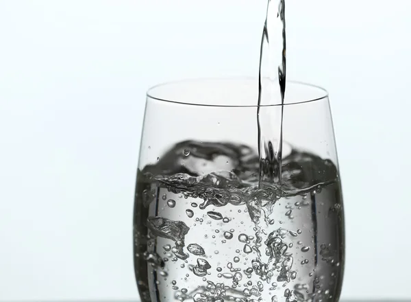 Verser l'eau de la bouteille sur le verre isolé sur blanc — Photo