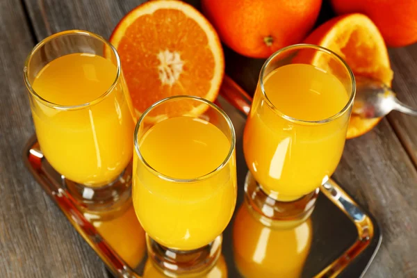 Glass of orange juice with slices on metal tray on rustic wooden background — Stock Photo, Image