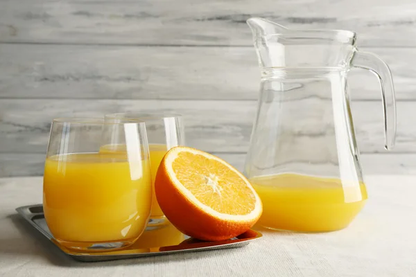 Vidro de suco de laranja com fatias na bandeja de metal na mesa com toalha de mesa e cor de fundo de parede de madeira — Fotografia de Stock