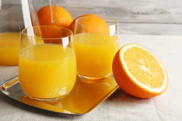 Vidro de suco de laranja com fatias na bandeja de metal na mesa com toalha de mesa e cor de fundo de parede de madeira — Fotografia de Stock