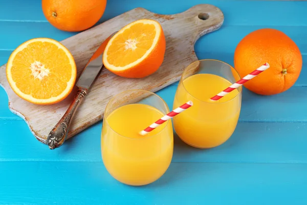 Bicchiere di succo d'arancia con cannucce e fette su tagliere con coltello su fondo di legno a colori — Foto Stock