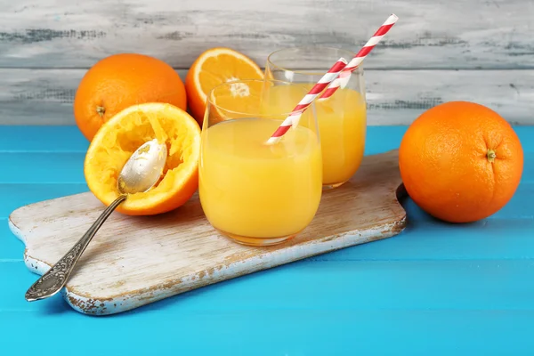 Vaso de zumo de naranja con pajitas, cuchara y rodajas en tabla de cortar sobre fondo de madera de color —  Fotos de Stock