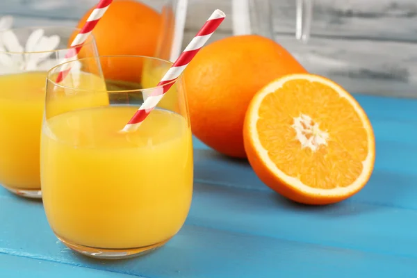 Copo de suco de laranja com fatias, flores e palhas sobre fundo de madeira cor — Fotografia de Stock