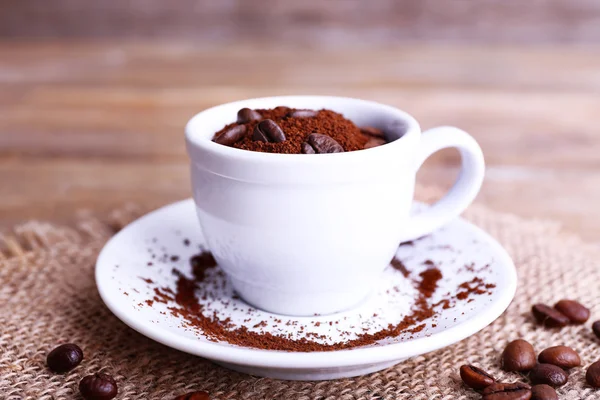 Mugg av kaffebönor och kaffe på säckväv på träbord på trä bakgrund — Stockfoto