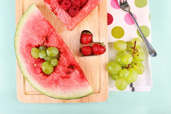 Fresh juicy watermelon slice  with cut out heart shape, filled fresh berries, on cutting board, on wooden background — Stock Photo, Image