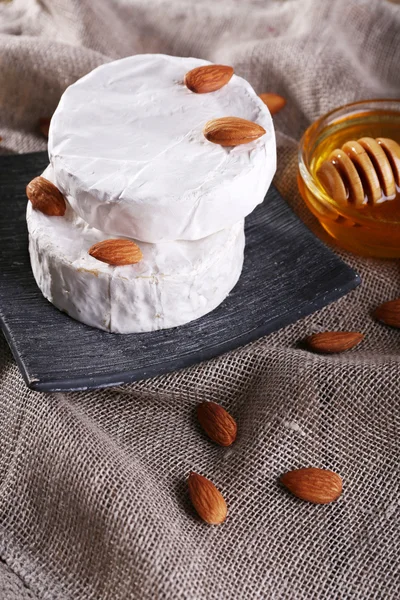 Camembert fromage sur assiette, miel dans un bol en verre et noix sur fond de sac — Photo