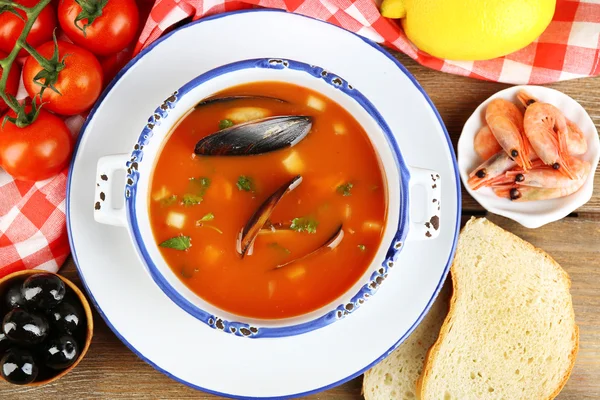 Tasty soup with mussels, tomatoes and black olives in bowl on wooden background — Stock Photo, Image