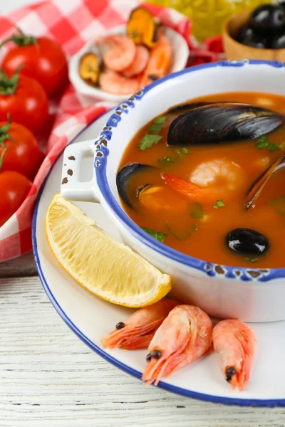 Tasty soup with shrimps, mussels, tomatoes and black olives in bowl on wooden background — Stock Photo, Image