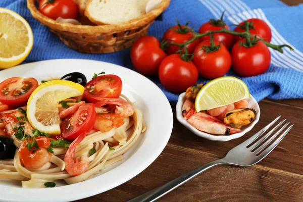 Tasty pasta with shrimps, mussels, black olives and tomato sauce on plate on wooden background — Stock Photo, Image