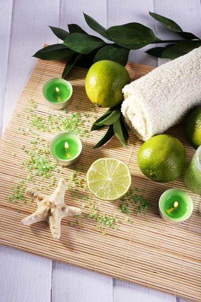 Composición del spa con cal, toalla y velas sobre estera de bambú y fondo de madera de color — Foto de Stock