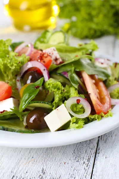 Griechischer Salat im Teller auf farbigem Holztischhintergrund — Stockfoto