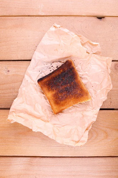 Burnt toasted bread on piece of paper and wooden table background — Stock Photo, Image
