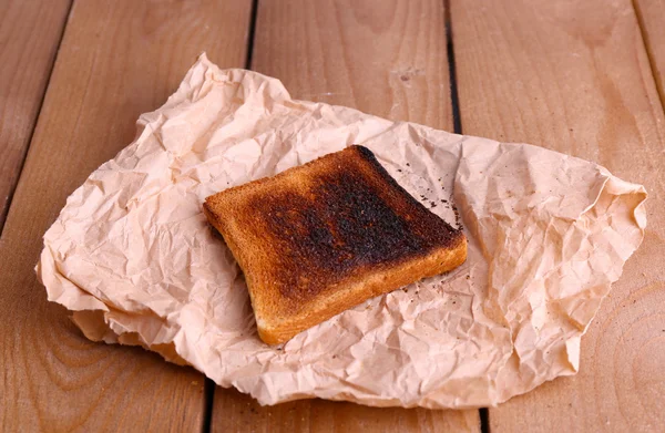 Burnt toasted bread on piece of paper and wooden table background — Stock Photo, Image