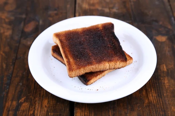 Pan tostado quemado en plato, sobre fondo de mesa de madera — Foto de Stock