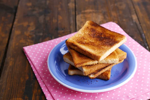 Ahşap masa arka plan üzerinde pembe peçete ile mavi plaka üzerinde tost ekmeği — Stok fotoğraf