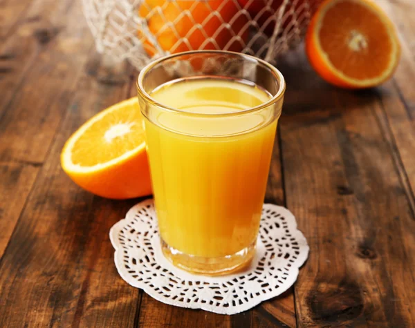 Glass of orange juice on lace doily with metal basket and slices on wooden table background — Stock Photo, Image