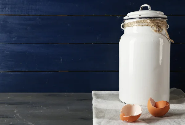 Milk can with eggshell on color wooden background — Stock Photo, Image