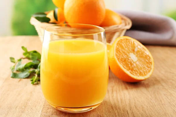Glas Orangensaft und Weidenkorb mit Orangen auf Holztisch und hellem Hintergrund — Stockfoto