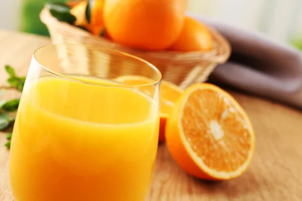 Copo de suco de laranja e cesta de vime com laranjas na mesa de madeira e fundo brilhante — Fotografia de Stock