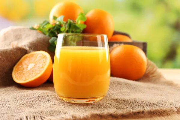 Glass of orange juice on wooden table with burlap cloth and bright background — Stock Photo, Image