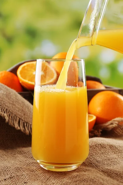 Pouring orange juice from glass carafe, on wooden table and bright background — Stock Photo, Image