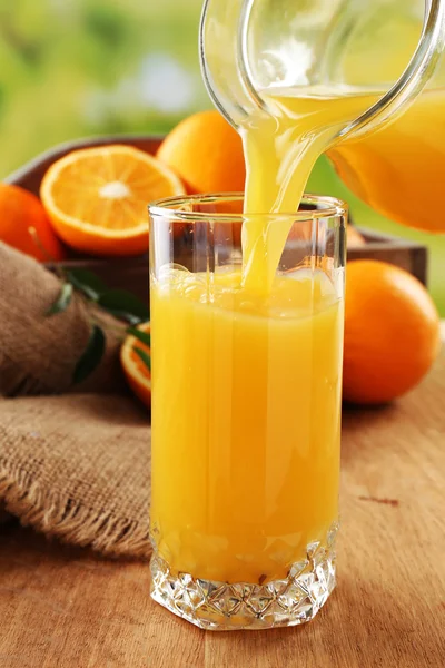 Pouring orange juice from glass carafe, on wooden table and bright background — Stock Photo, Image