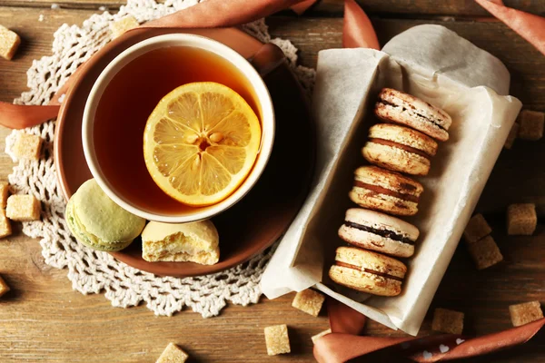 Makaroni berwarna dengan secangkir teh di latar belakang kayu — Stok Foto