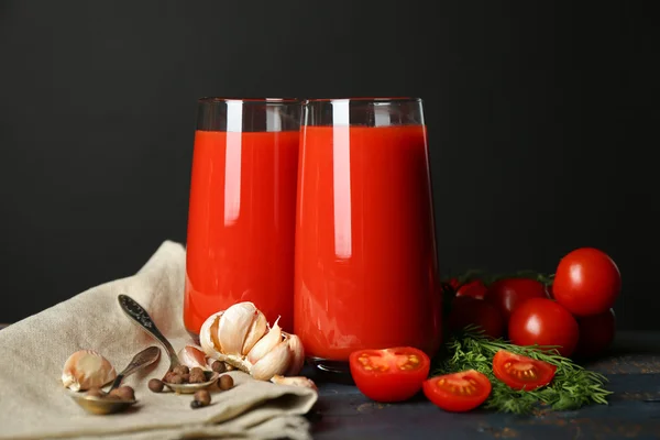 Gläser mit leckerem Tomatensaft und frischen Tomaten auf dem Tisch, auf grauem Hintergrund — Stockfoto