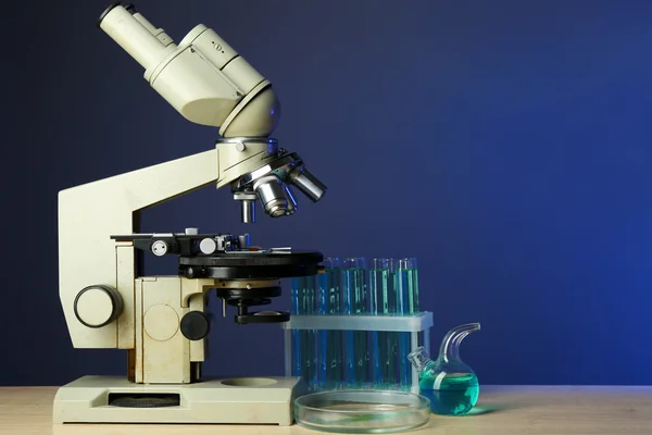 Microscópio e tubos de ensaio na mesa, sobre fundo de cor — Fotografia de Stock