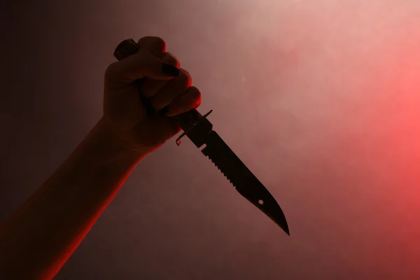 Női kezében kés piros háttér — Stock Fotó