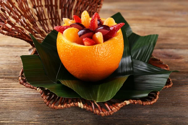 Fruit dessert in orange peel on green leaf on table — Stock Photo, Image