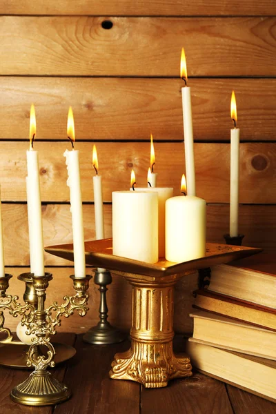 Retro candlesticks with candles and books, on wooden background Stock Image
