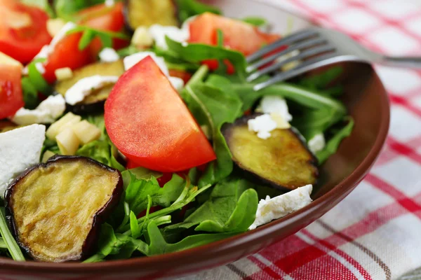 Eggplant salad with tomatoes, arugula and feta cheese, on napkin, on color wooden background — Stock Photo, Image