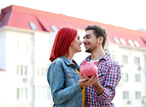 Loving couple with piggy bank near apartment house