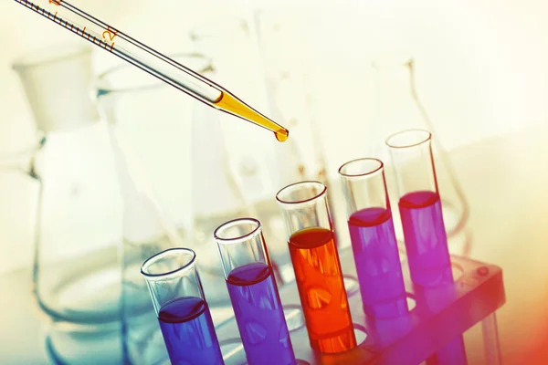 Pipette adding yellow fluid to one of several test-tubes with flasks on light background — Stock Photo, Image