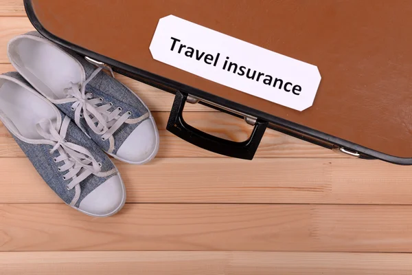 Reisekoffer mit Aufschrift Reiseversicherung auf Holzgrund — Stockfoto