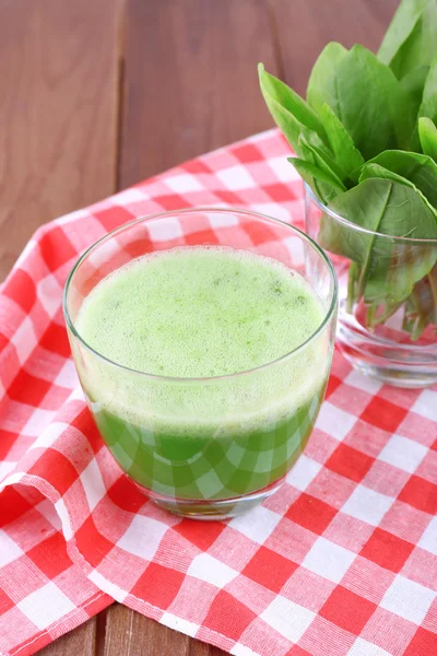 Glass of green smoothie and glassware of spinach on napkin, on wooden table background — Stock Photo, Image