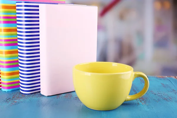 Taza de té de color con libros en la mesa, sobre fondo claro borroso — Foto de Stock