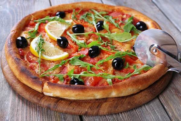 Gustosa pizza con erbe aromatiche e coltello rotondo a bordo e sfondo tavolo in legno — Foto Stock