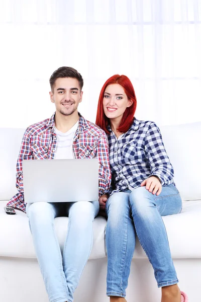 Pareja joven sentada en sofá con portátil en la habitación — Foto de Stock