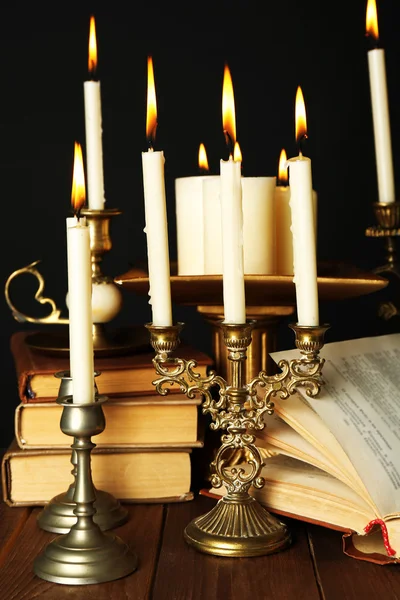 Candelabros retro con velas y libros, sobre mesa de madera, sobre fondo negro — Foto de Stock