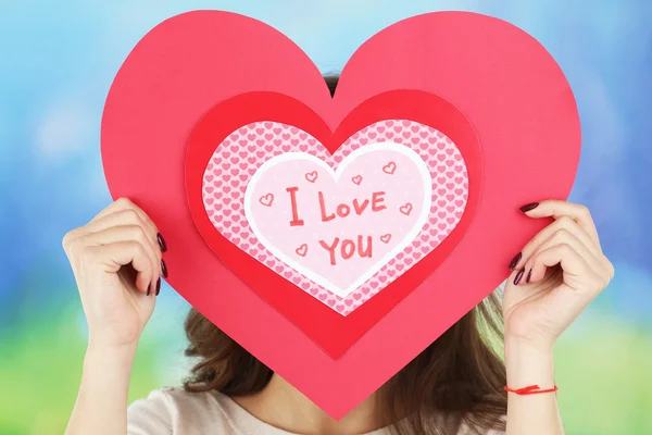 Girl holding Valentine card on bright background — Stock Photo, Image